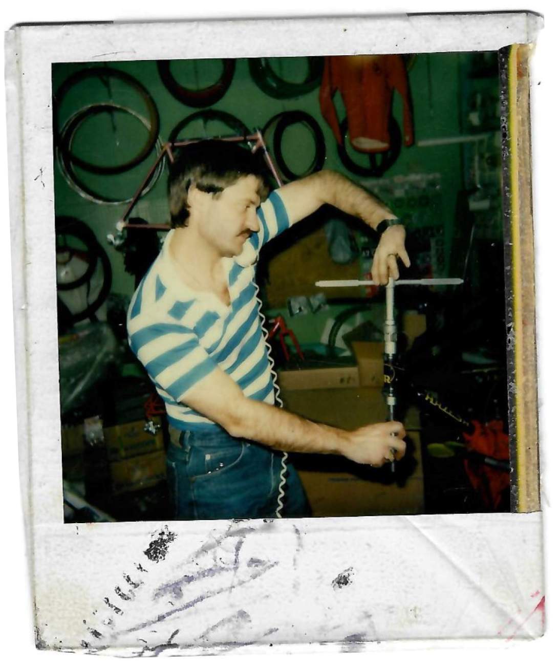 Polaroid photograph of Philip Cabbad building a bicycle by hand in the R&A Cycles workshop, tires hanging on the wall behind him, circa late 1970s